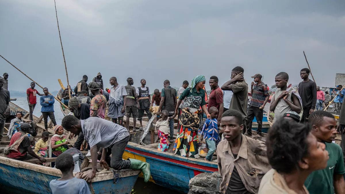 Survivors and local residents gather near wooden boats along the Congo River following a maritime disaster, waiting for rescue or aid.
