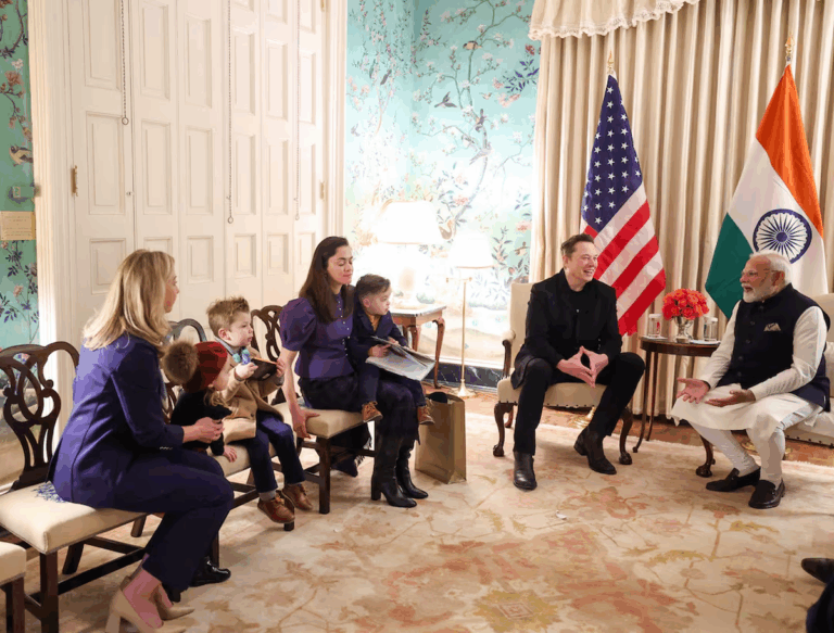 Indian Prime Minister Narendra Modi meeting with Elon Musk and his family in a formal setting, with U.S. and Indian flags in the background.