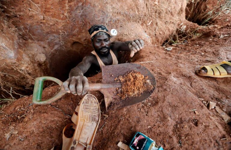 Miner in Africa emerges from a narrow pit, handing up a shovel full of raw earth, symbolizing the grueling labor behind Africa's mineral exports.