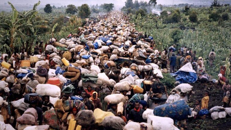 Thousands of displaced Congolese civilians carry belongings on foot through a rural road, highlighting mass displacement.