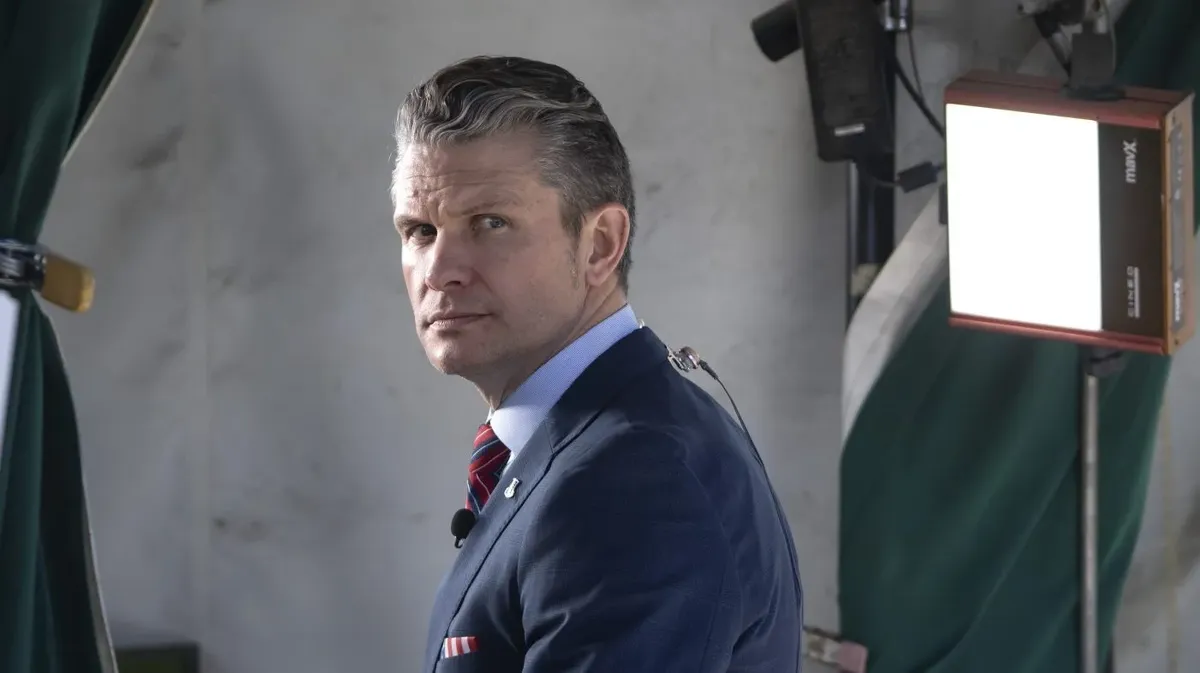 U.S. Defense Secretary Pete Hegseth looks over his shoulder while preparing for a broadcast interview, with studio lights in the background.