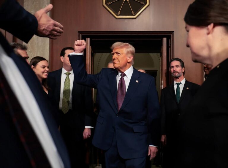 Former President Donald Trump raises his fist while entering a chamber surrounded by lawmakers, as a clock overhead symbolizes his daylight saving time push.