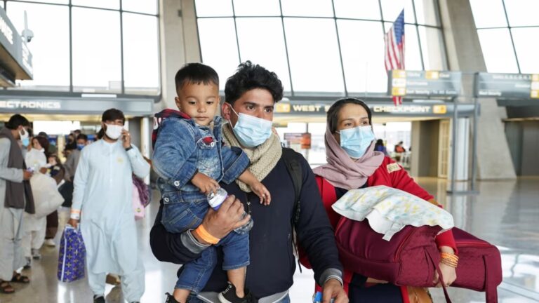 A young Afghan family walks through a U.S. airport as Afghan deportation protection ends under Trump’s immigration policy.