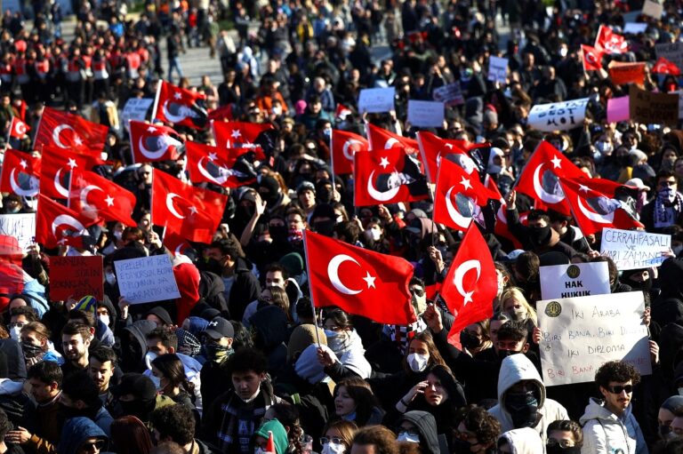 Large crowd waving Turkish flags during May Day arrests in Istanbul, holding protest signs and marching through the city