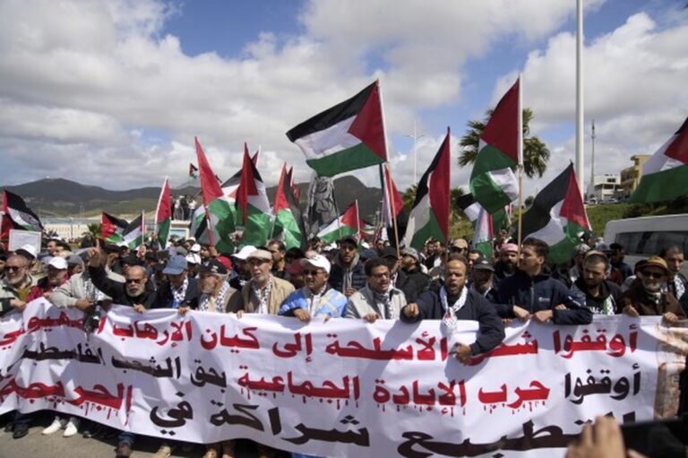 Protesters in Morocco hold a large banner and wave Palestinian flags during a demonstration against Morocco-Israel relations.