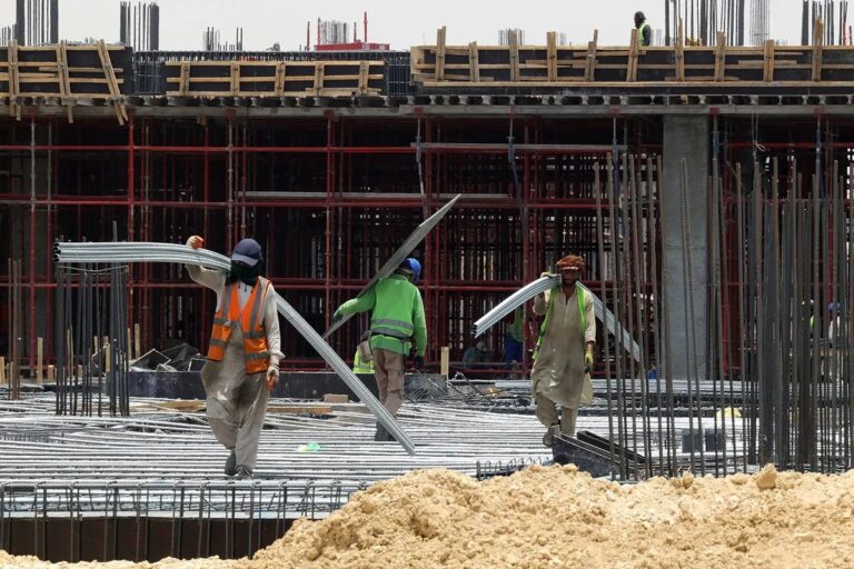 Migrant workers carry metal beams across an active construction site in Saudi Arabia amid growing concern over World Cup construction deaths.